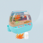 A children's toy aquarium with a light blue base, clear domed top, and colorful underwater decorations including orange coral, green seaweed, and small fish, shown on a pale blue background.